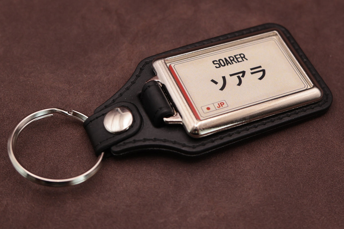 Toyota Soarer Katakana keyring angled with the split ring at lower left, showing the cream insert and black leatherette fob