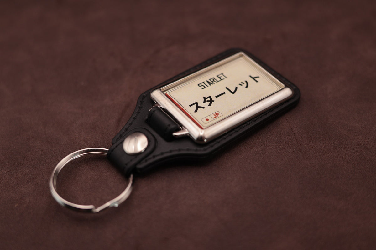 Toyota Starlet Katakana keyring angled with the split ring at lower left, showing the cream insert and black leatherette fob