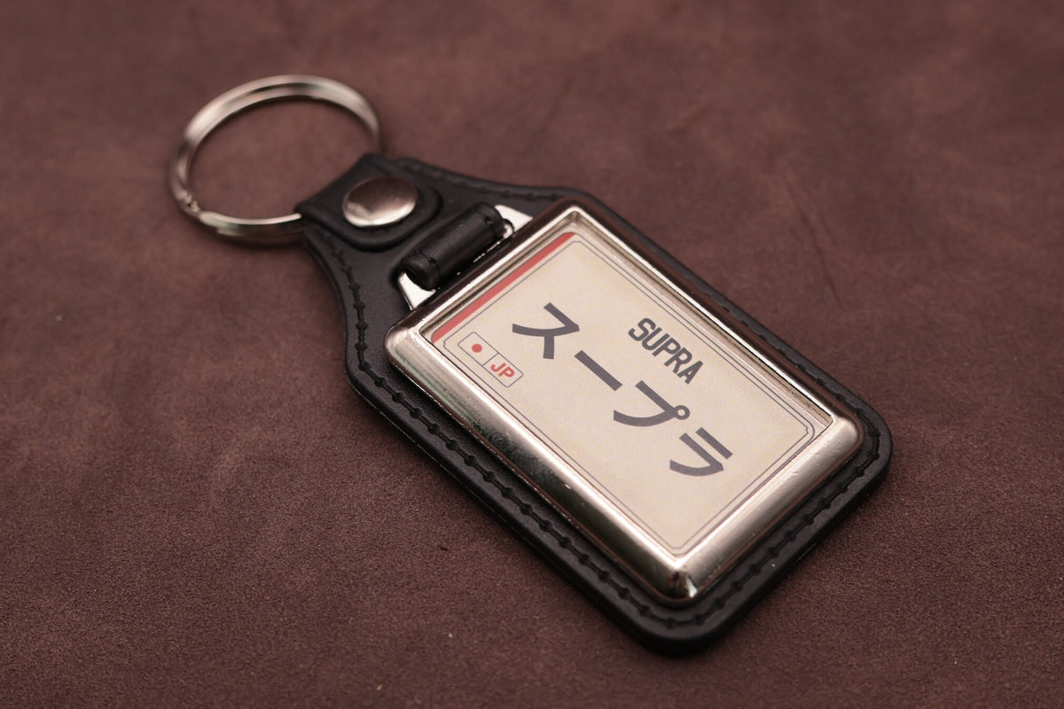 Toyota Supra Katakana keyring angled with the split ring at upper left, showing the printed insert and chromed frame