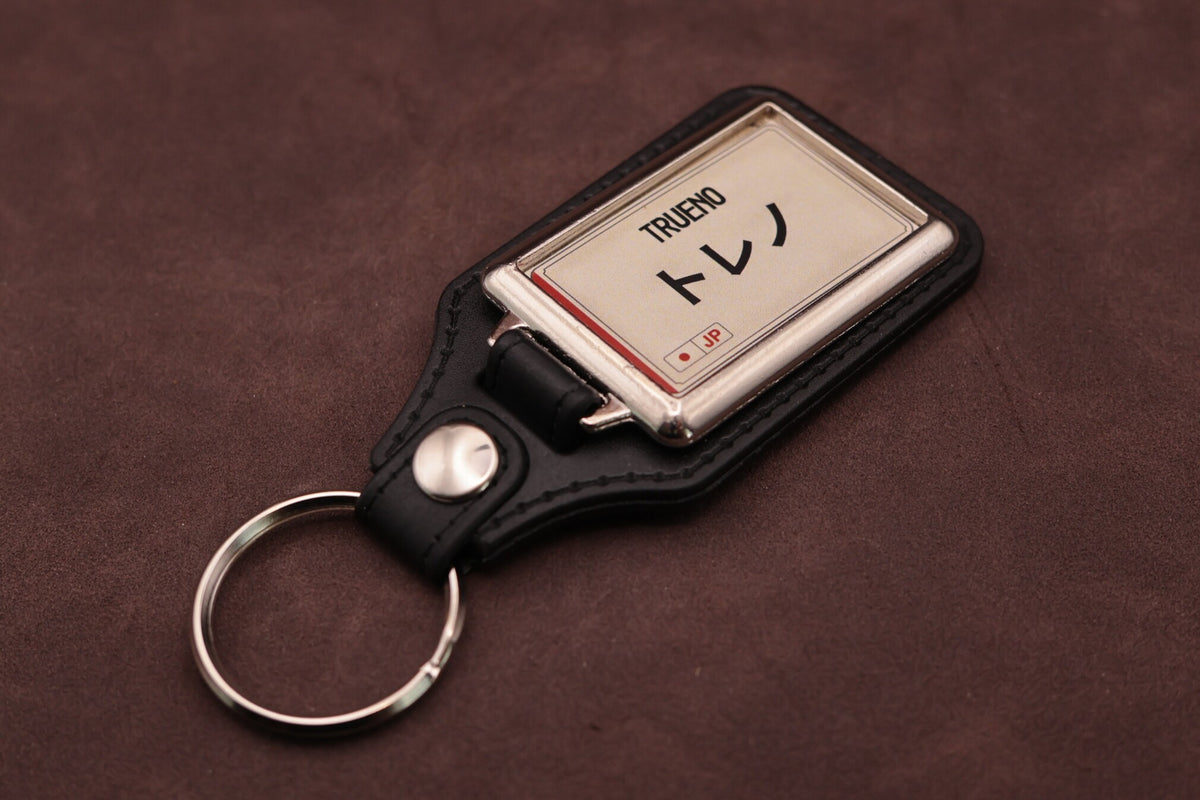 Toyota Trueno Katakana keyring angled with the split ring at lower left, showing the cream insert and black leatherette fob