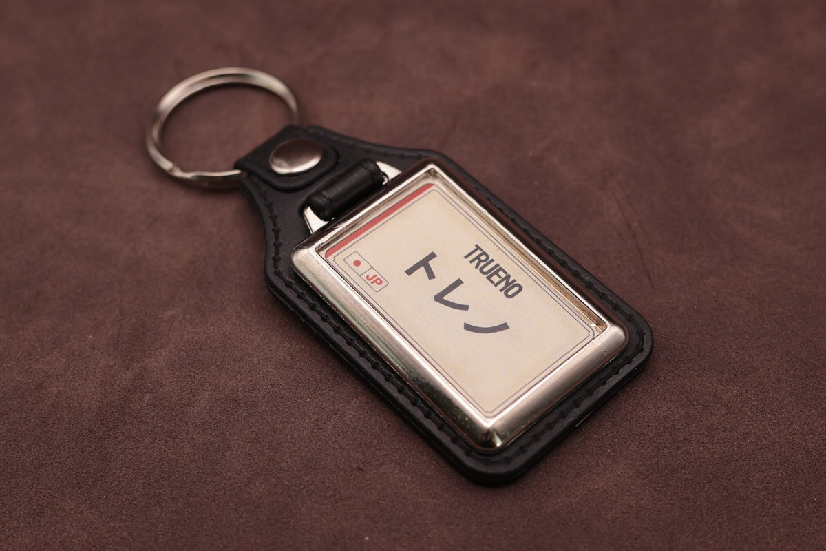 Toyota Trueno Katakana keyring angled with the split ring at upper left, showing the printed insert and chromed frame